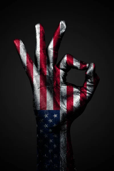 Ένα χέρι με μια σημαία των ΗΠΑ δείχνει ένα OK πινακίδα σε ένα σκοτεινό φόντο — Φωτογραφία Αρχείου