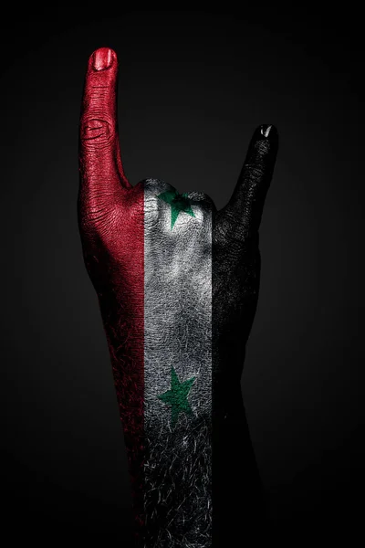 Una mano con una bandera de Siria dibujada muestra un signo de cabra, un símbolo de la música mainstream, metal y rock, sobre un fondo oscuro . —  Fotos de Stock