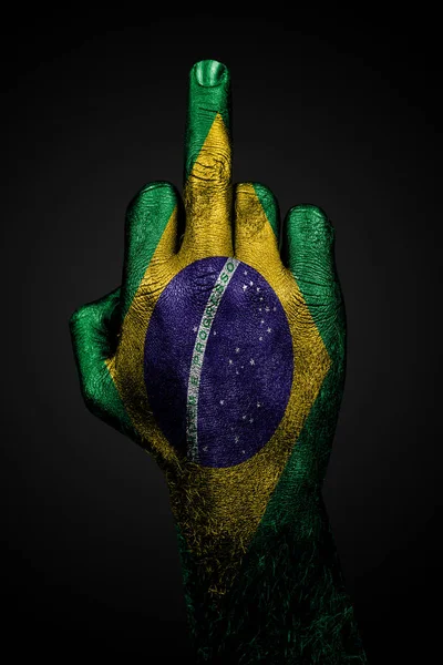 ブラジルの塗装された旗を持つ手は、暗い背景に対して、中指、侵略の兆候を示しています. — ストック写真