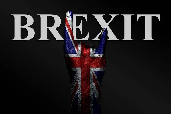 På en mørk bakgrunn viser en hånd med et malt britisk flagg og ordet BREXIT et geitetegn, et symbol på mainstream, metall og rockemusikk . – stockfoto
