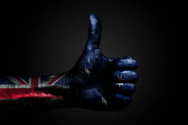 A hand with a drawn Australia flag shows a finger up sign, a symbol of success, readiness, a task done on a dark background.