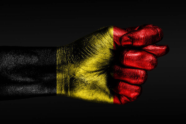 A hand with a painted Belgium flag shows a fig, a sign of aggression, disagreement, a dispute on a dark background.