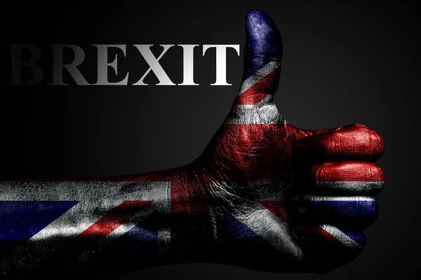 En hånd med et malt britisk flagg viser et "tommel opp" skilt og inskripsjonen BREXIT, et symbol på suksess, beredskap, og en oppgave utført på mørk bakgrunn . – stockfoto