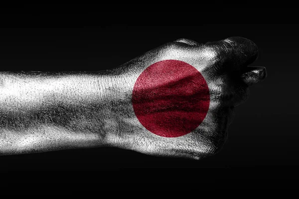 Une main avec un drapeau peint du Japon montre une figue, un signe d'agression, un désaccord, une dispute sur un fond sombre . — Photo