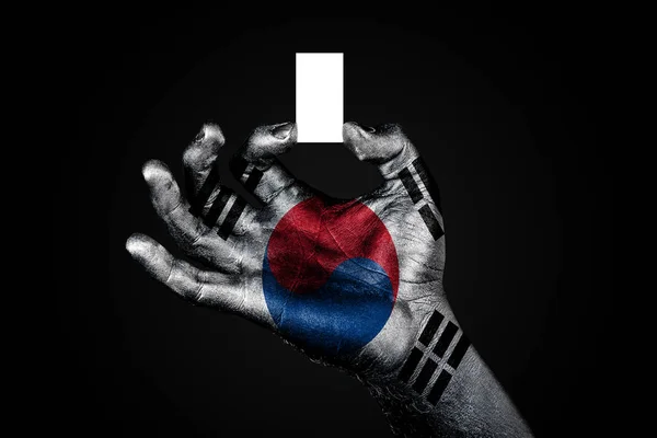 Mano con una bandiera dipinta Corea del Sud che tiene un piccolo foglio bianco con spazio per un'iscrizione, finto — Foto Stock