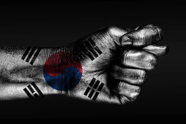 Una mano con una Corea del Sur pintada, bandera muestra un higo, un signo de agresión, desacuerdo, una disputa sobre un fondo oscuro . — Foto de Stock