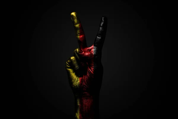 A hand with a drawn Germany flag shows an PEACE sign, a symbol of peace, friendship, greetings and peacefulness on a dark background.