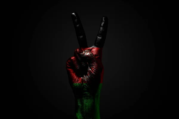 A hand with a drawn Afghanistan flag shows an PEACE sign, a symbol of peace, friendship, greetings and peacefulness on a dark background. — Stock Photo, Image