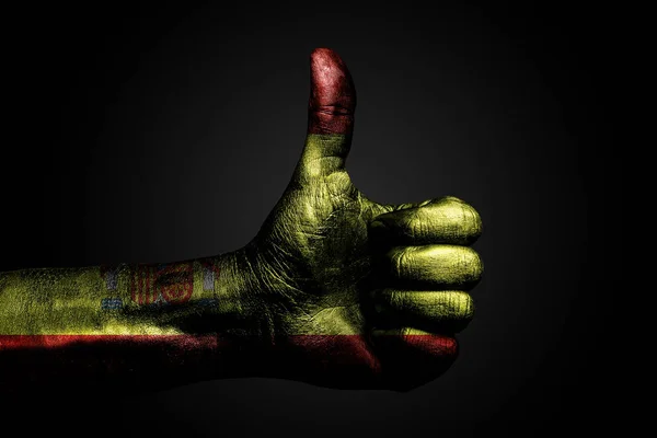 A hand with a drawn Spain flag shows a finger up sign, a symbol of success, readiness, a task done on a dark background.