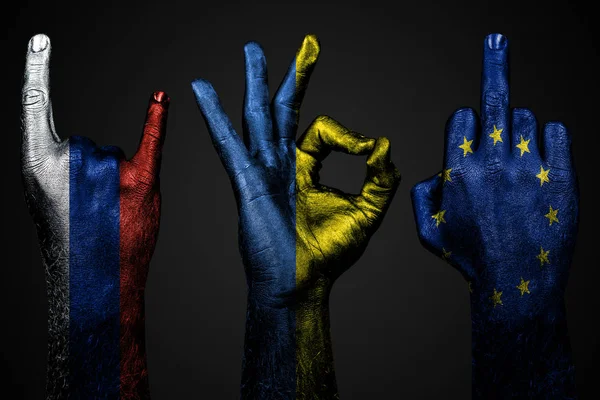 Een set van drie handen met een geschilderde vlag van Oekraïne, Rusland en de Europese Unie tonen middelvinger, geit en Oke, een teken van agressie, protest en goedkeuring op een donkere achtergrond. — Stockfoto