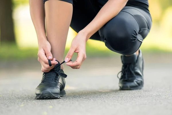 Женские руки завязывают черные кроссовки, символ подготовки к бегу или спорту — стоковое фото