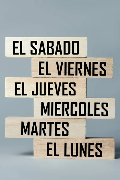 A list of wooden blocks lying on top of each other with a list of six-day working week days in Spanish. Vertical frame