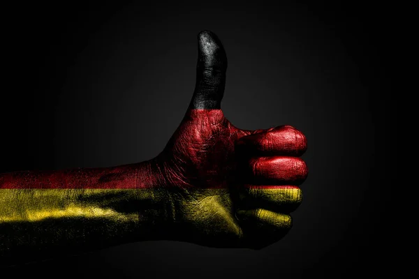 Een hand met een getekende Duitsland vlag toont een vinger omhoog teken, een symbool van succes, gereedheid, een taak gedaan op een donkere achtergrond. — Stockfoto