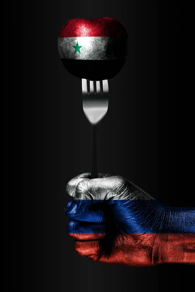 Una mano con una bandera de Rusia dibujada sostiene un tenedor, en el que hay una pelota con una bandera de Siria dibujada, un signo de influencia, presión, agarre y anecxia. . —  Fotos de Stock