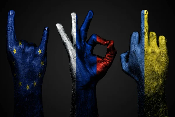 Набір з трьох рук з розписним прапором України, Росією і Європейським Союзом показує середній палець, Коза і добре, ознака агресії, протест і схвалення на темному фоні. — стокове фото