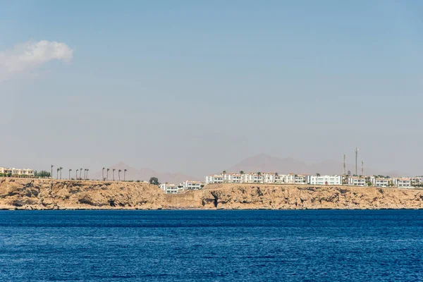 hotels and houses in the distance stand over a cliff above the blue sea.