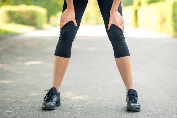 Женские ноги с крупным планом рук в них, символ усталости после бега или спортивных мероприятий — стоковое фото