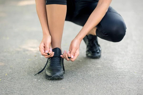 女人们的手把黑色运动鞋系上带子，作为跑步或运动准备的象征 — 图库照片