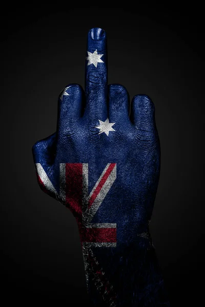 Uma mão com uma bandeira pintada da Austrália mostra o dedo médio, um sinal de agressão, contra um fundo escuro . — Fotografia de Stock