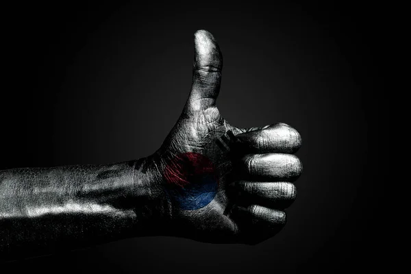 Een hand met een getekende Zuid-Korea vlag toont een vinger omhoog teken, een symbool van succes, gereedheid, een taak gedaan op een donkere achtergrond. — Stockfoto