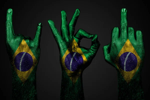 Um conjunto de três mãos com uma bandeira pintada Brasil mostrar dedo médio, cabra e Ok, um sinal de agressão, protesto e aprovação em um fundo escuro . — Fotografia de Stock