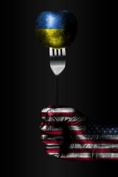 Une main avec un drapeau américain dessiné tient une fourchette, sur laquelle se trouve une balle avec un drapeau ukrainien dessiné, un signe d'influence, de pression, d'adhérence et d'anecxie . — Photo