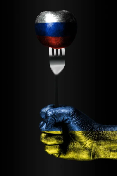Рука з намальований прапором України тримає виделку, на якій знаходиться кулька з намальований прапором Росії, ознакою впливу, тиску, зчеплення і anecxia. — стокове фото