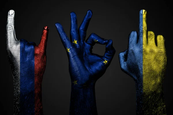 Un conjunto de tres manos con una bandera pintada de Ucrania, Rusia y la Unión Europea muestran el dedo medio, cabra y bien, un signo de agresión, protesta y aprobación sobre un fondo oscuro . — Foto de Stock