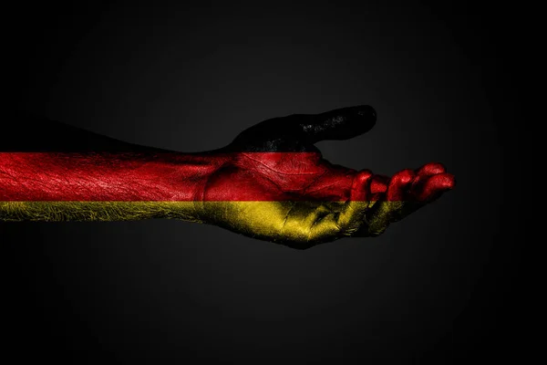 Ausgestreckte Hand mit einer gezogenen Deutschland-Fahne, einem Zeichen der Hilfe oder einer Bitte, auf dunklem Hintergrund. — Stockfoto