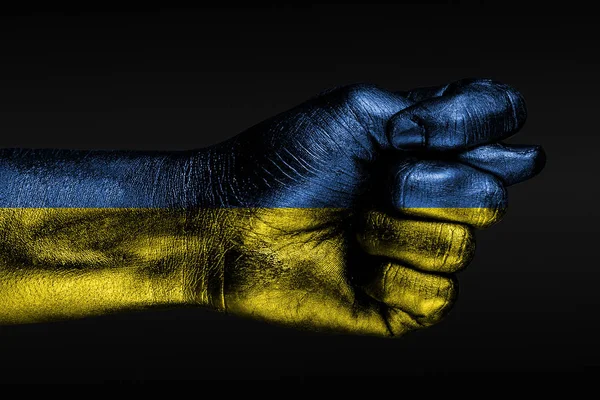 Une main avec un drapeau peint de l'Ukraine montre une figue, un signe d'agression, un désaccord, un différend sur un fond sombre . — Photo