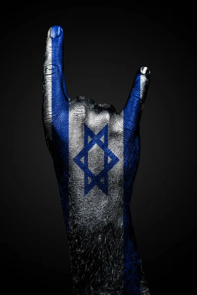 Una mano con una bandera de Israel dibujada muestra un signo de cabra, un símbolo de la música mainstream, metal y rock, sobre un fondo oscuro . —  Fotos de Stock