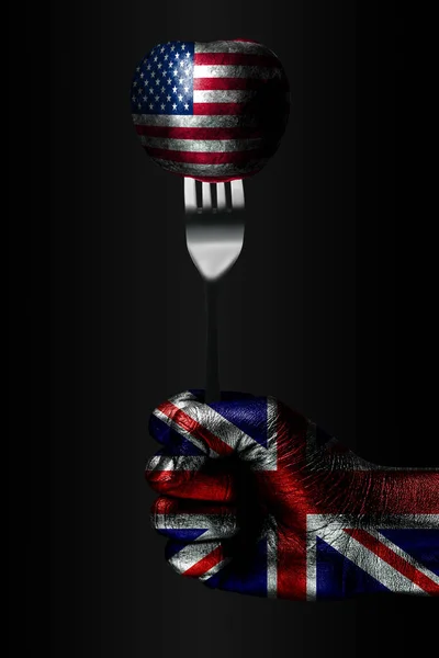 A hand with a drawn Great Britain flag holds a fork, on which is a ball with a drawn USA flag, a sign of influence, pressure, grip and anecxia.