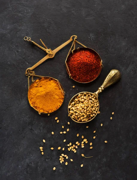 Spice powder turmeric and chili red powder  on brass scales and coriander seeds top view flat lay on black concrete background