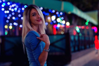 Sarışın bir kadın uzun saçlı ve mavi elbiseli güzel bir ince rakam. Portre karşı gece şehrin ışıkları.