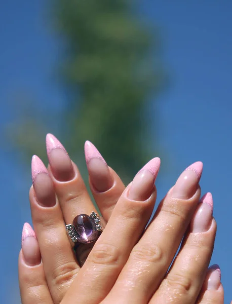 Long French nails with white manicure on a woman\'s hand with pink accessory on a nature background.