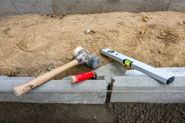 Setting edge restraints buy putting border curb stones in earth-moist concrete with rubber mallet, trowel and bubble level