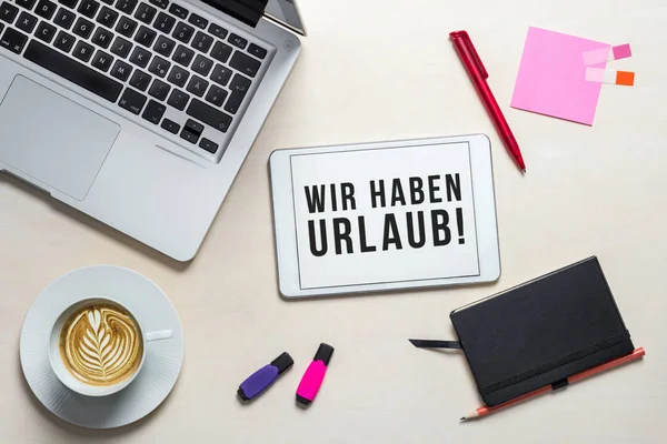 Wir haben Urlaub yukarıdan flatlay dizüstü bilgisayar ile bir ofis resepsiyon arka plan olarak tatil için kapalı anlam tablet Almanca yazılmış