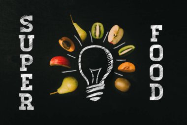 Şablon olarak taze sağlıklı kesim meyve tarafından çevrili kara kara tahta üzerinde tebeşir beyaz ışık ampul ile yazılan superfood boyalı