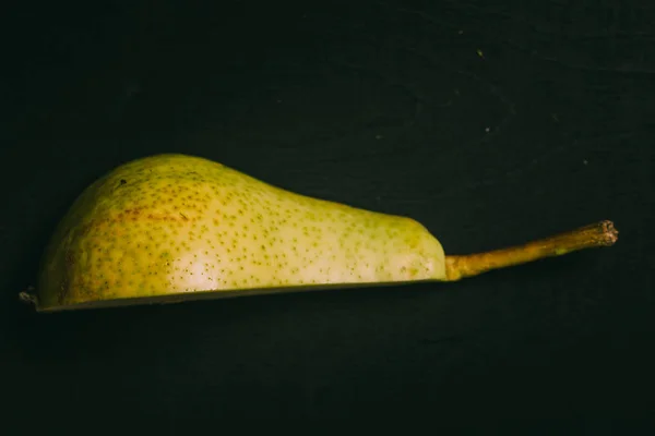 Cut pear lying on black chalkboard in background with copy space from above as flat lay