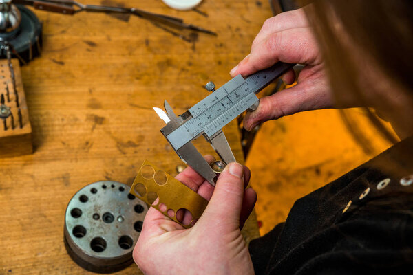 Working and scaling a jewelry piece at workshop with aid of suiting equipment and goldsmith standing and holding with both hands