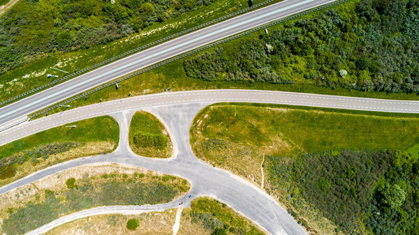 Curved road and bicycle lane surrounded by green grass and trees taken from above with drone 