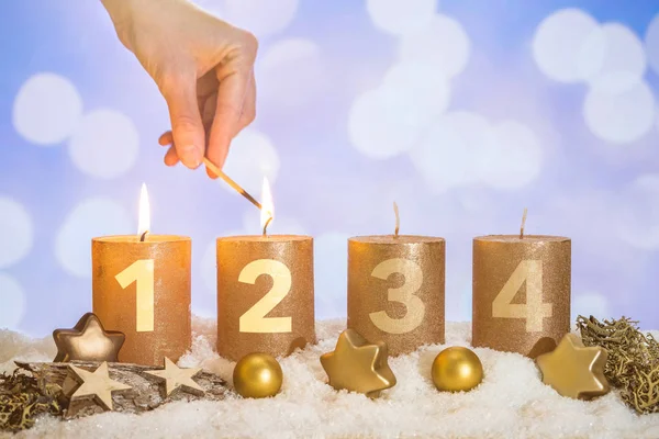 Four numbered gold advent candles with two candles lit by hand with match and christmas decoration lying in snow as template