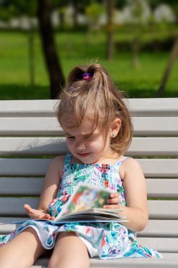 küçük kız parkta bir bankta oturur ve yaz günü kitap okur