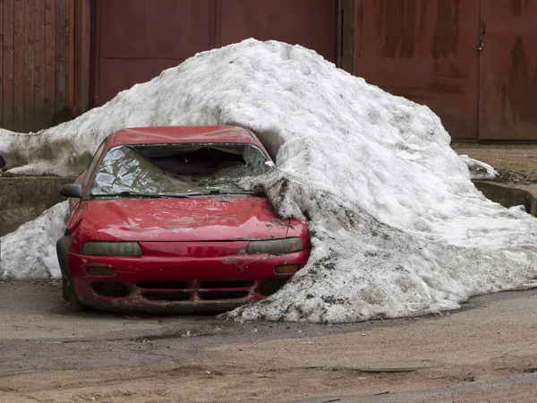 O velho carro meio arruinado no quintal sob neve não descongelada — Fotografia de Stock