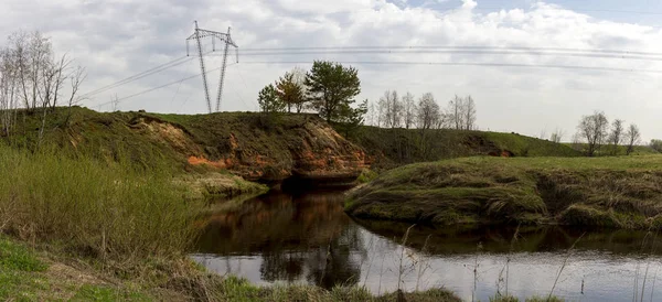 Панорама скрученого різкого узбережжя маленької річки з лініями електропередач — стокове фото