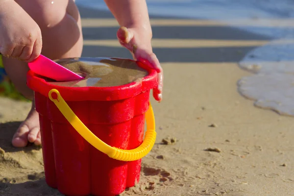 Il bambino gioca con un secchio e sabbia sulla riva del mare in giorno d'estate — Foto Stock