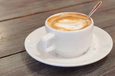 Kafedeki ahşap bir masada kapuçino bardağı.