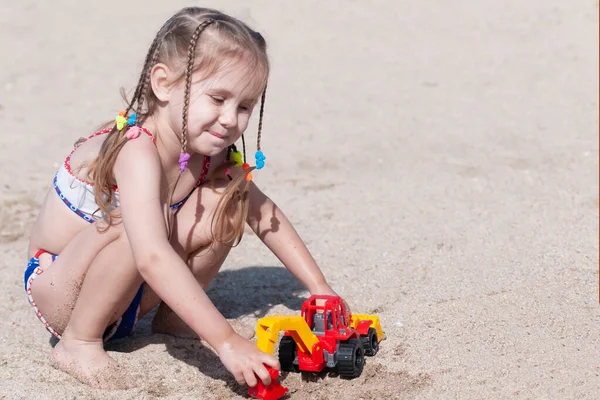 3歳の少女は夏の晴れた日に砂浜で機械と遊ぶ — ストック写真