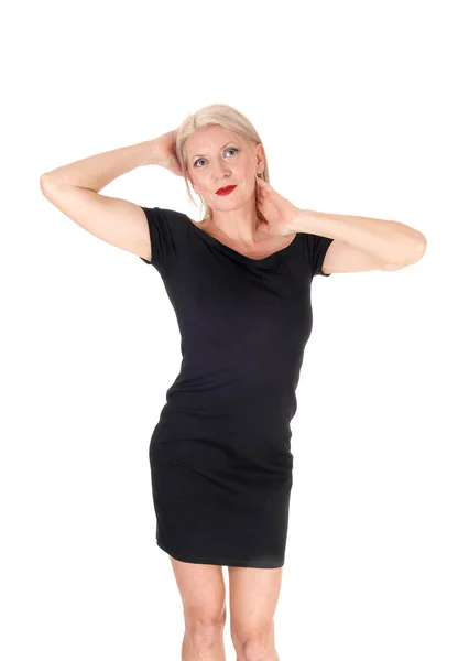 Красива жінка стоїть в короткій чорній сукні руки на голові — стокове фото