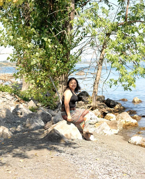 Mujer feliz agradable sentado en el lago bajo algunos árboles — Foto de Stock